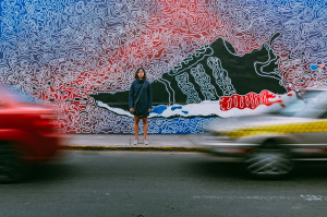 Urban Motion: Woman Amidst Vibrant Street Art and Passing Vehicles